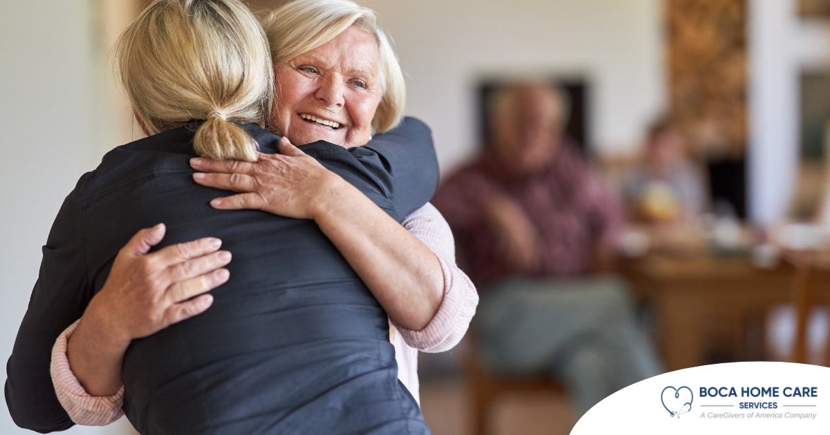 An older woman smiles as a younger woman visits her and hugs her, showing the effect that acts of kindness can have on senior loved ones.