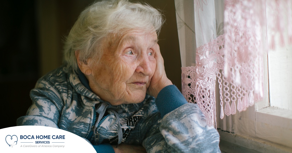 An older woman peacefully looks out of the window while the sun is still up, representing what can happen with sundowning.